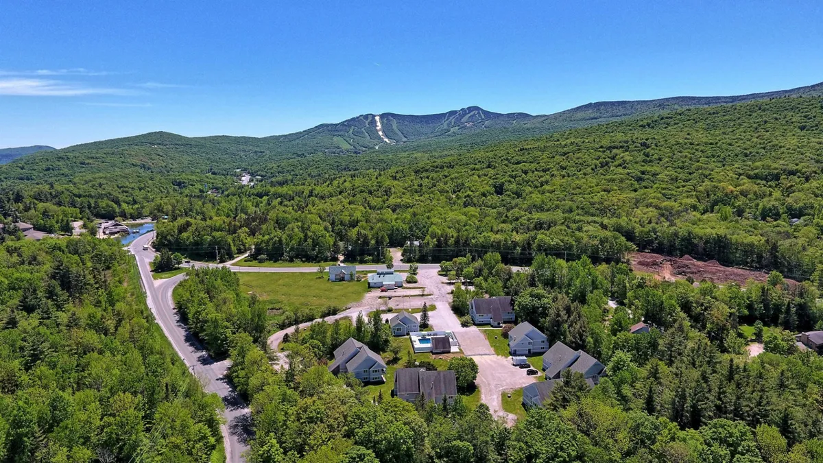 This exterior shot presents a scenic view of mountains in the background, with a cluster of houses and a winding road leading into the landscape. The imagery suggests adventure and easy access to outdoor recreation—ideal for those eager to hit the slopes or explore the surrounding nature.