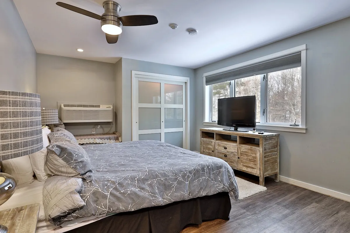 A cozy bedroom featuring a plush bed, a window that lets in natural light, a smart TV mounted for easy viewing from bed, and a convenient dresser. The room offers a restful and private space for relaxation, ideal for unwinding after a day of activity.