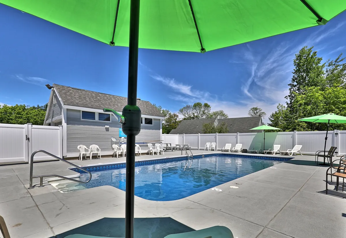 This exterior image features a sparkling swimming pool surrounded by green umbrellas and comfortable lounge chairs. The pool area is inviting and lively, with space for sunbathing, swimming, and outdoor relaxation. The bright atmosphere and well-maintained setting suggest a perfect spot for unwinding after a productive work session or socializing with others during downtime.