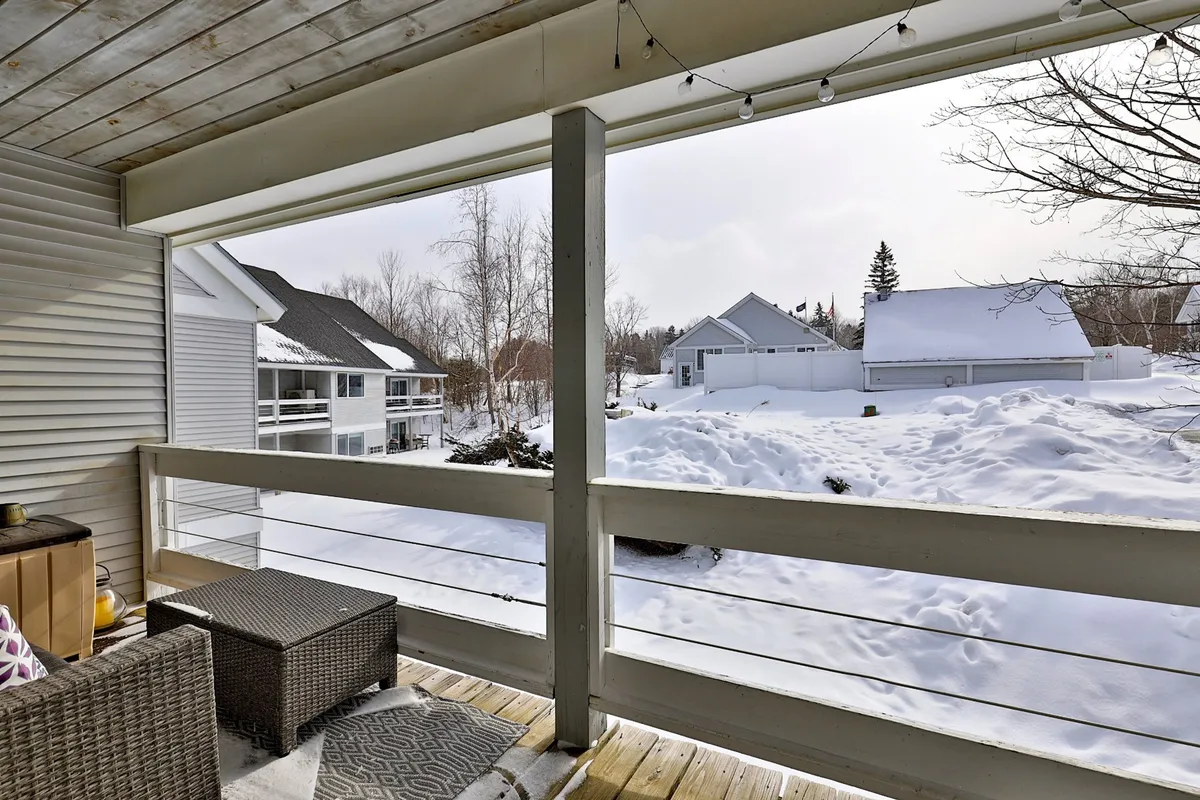 The image captures a snow-covered landscape featuring neighboring houses and an inviting outdoor seating area. The calm winter setting evokes the quintessential après-ski atmosphere, where guests can watch snowflakes fall and enjoy serene mountain views from the comfort of their condo's balcony or patio.