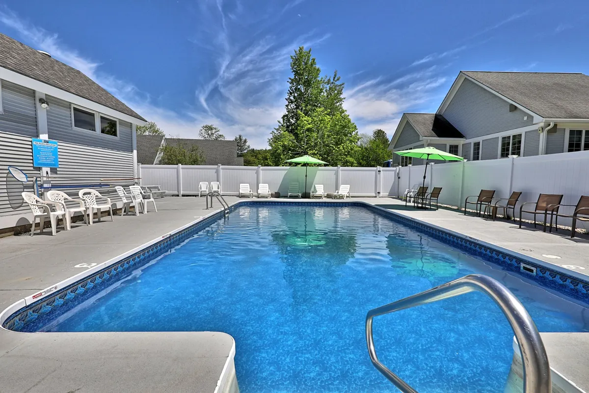 A vibrant outdoor swimming pool surrounded by lounge chairs and umbrellas, with lush greenery creating a resort-like atmosphere. The relaxed mood invites guests to swim, sunbathe, or socialize beside the pool.