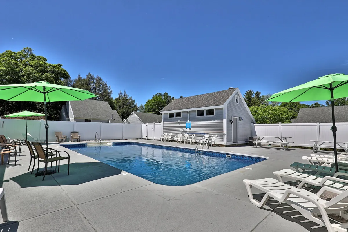 Another view of the exterior pool area, this time highlighting the white fence, pool house, and additional lounge chairs. The scene evokes leisurely afternoons, social gatherings, and a cheerful ambiance, with the pool as a central feature for recreation and relaxation.