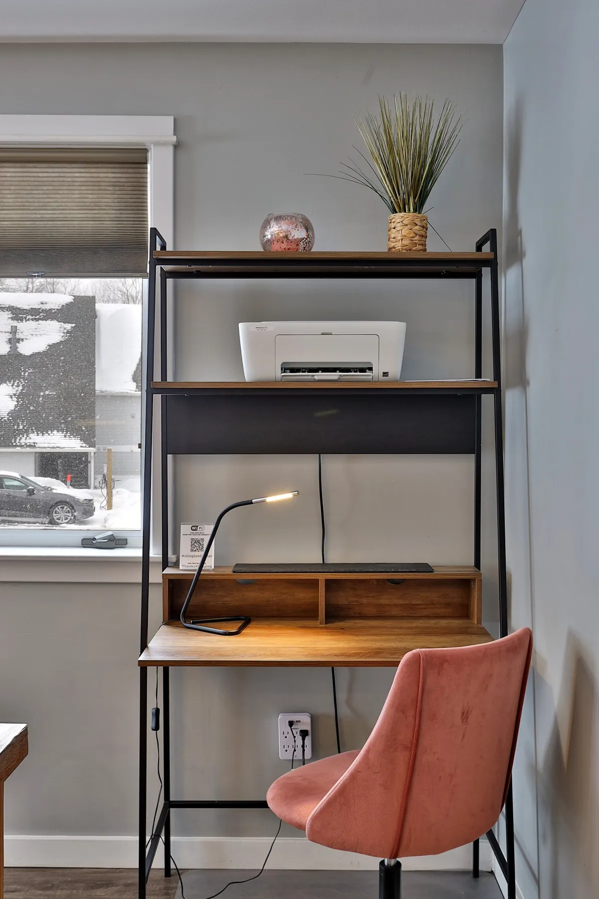 A compact, well-lit workspace with a sleek desk, comfortable chair, shelves, lamp, and printer, situated conveniently within the living area. The setup is functional and inviting, catering to productivity without sacrificing the welcoming atmosphere of the home.