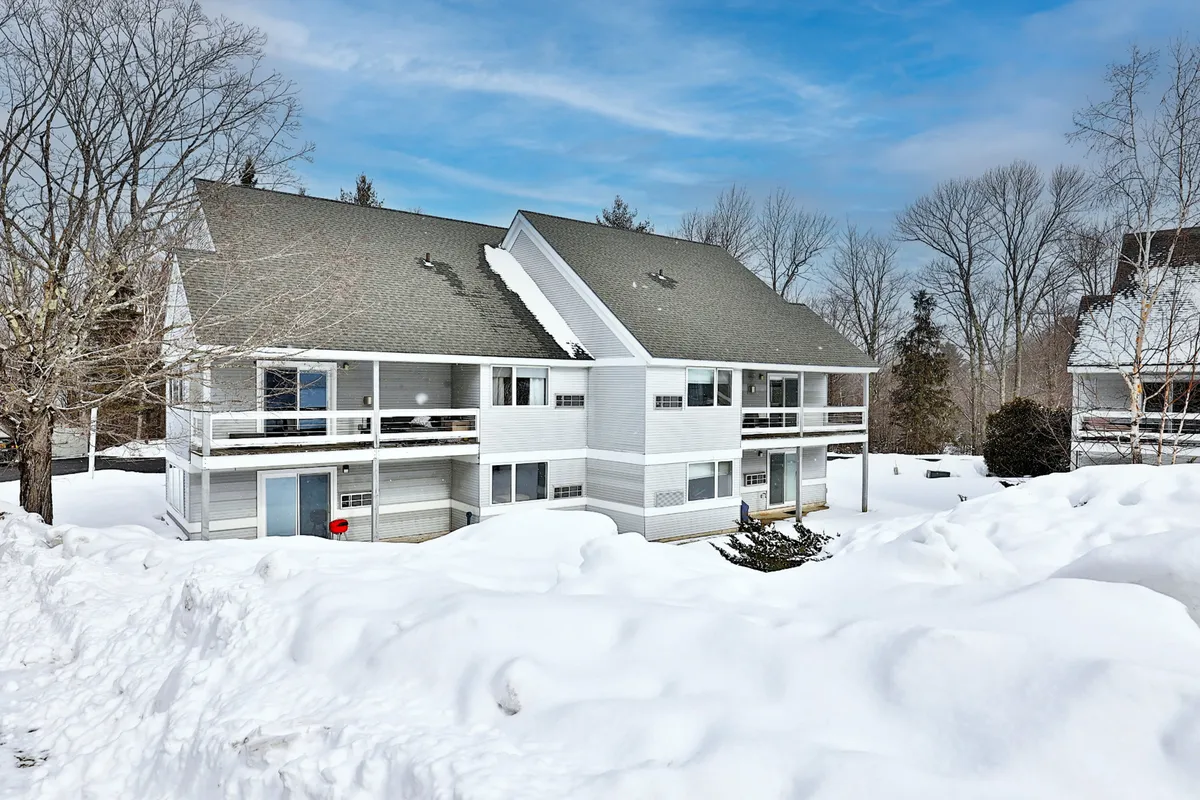 A two-story building set against a snow-covered landscape and tree line, evoking the calm and beauty of winter. The balconies and setting suggest easy access to the outdoors, reflecting the region's seasonal appeal.